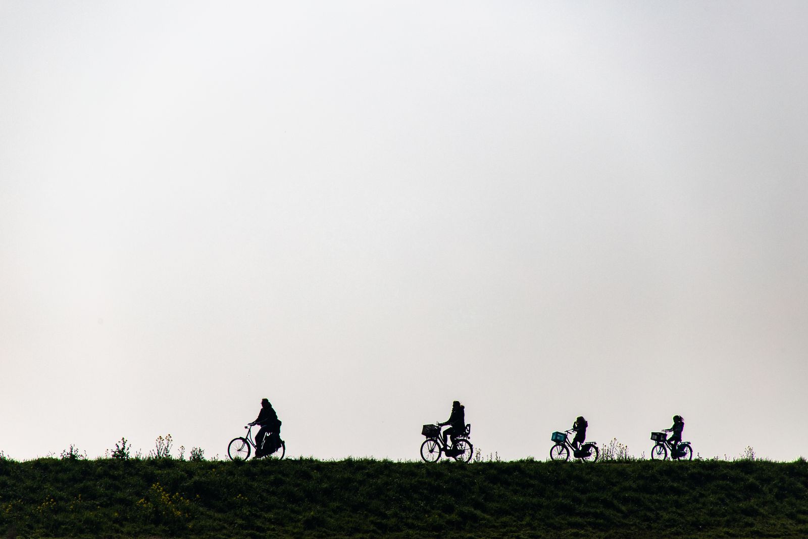 Een gezin fietst achter elkaar over een dijk bij Marken, als silhouetten tegen de lucht.