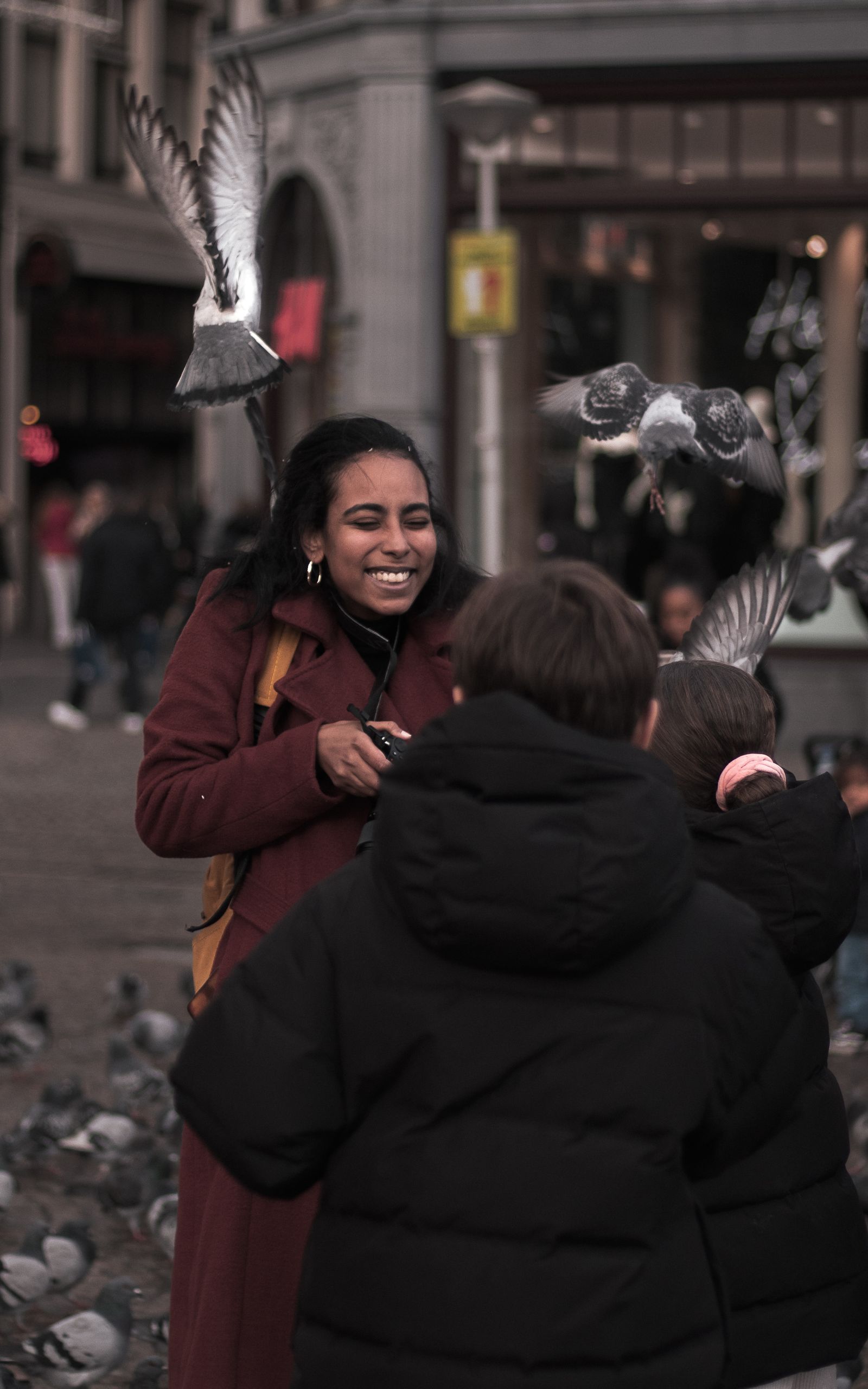 Een moeder lacht met haar kinderen tussen opvliegende duiven op een Amsterdams plein.