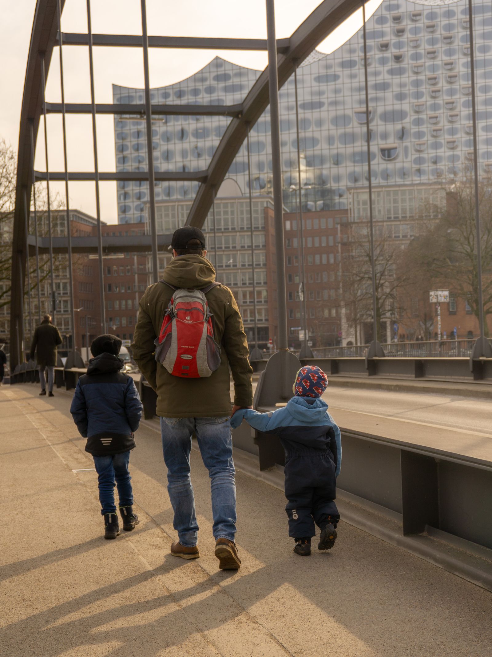 Een vader wandelt hand in hand met zijn twee kinderen over een brug in Hamburg.